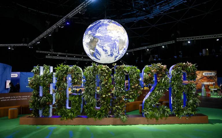 Photo from the 'Blue Zone' at COP26, a glowing globe of the earth hangs above giant letters adorned with greenery, spelling #COP26.