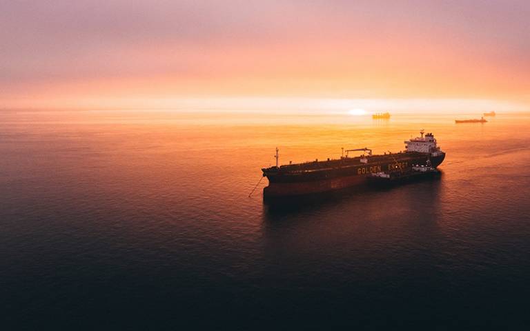 Photo shows freight ship in the sea against a sunset background.
