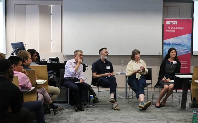 A panel of two men and two women are sitting at the front of a lecture hall, listening to an audience member asking a question during a panel discussion at the symposium..