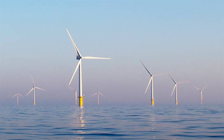 A row of wind turbines in the sea, against a pink and blue sky