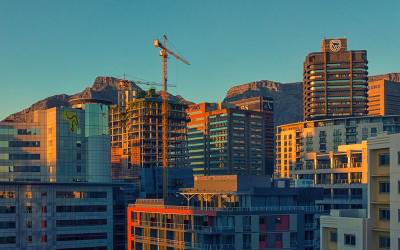 High-rise buildings being constructed. The background is a blue sky with mountains.