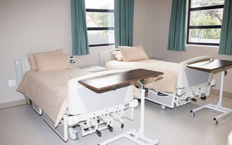 Two hospital beds in a room with two windows