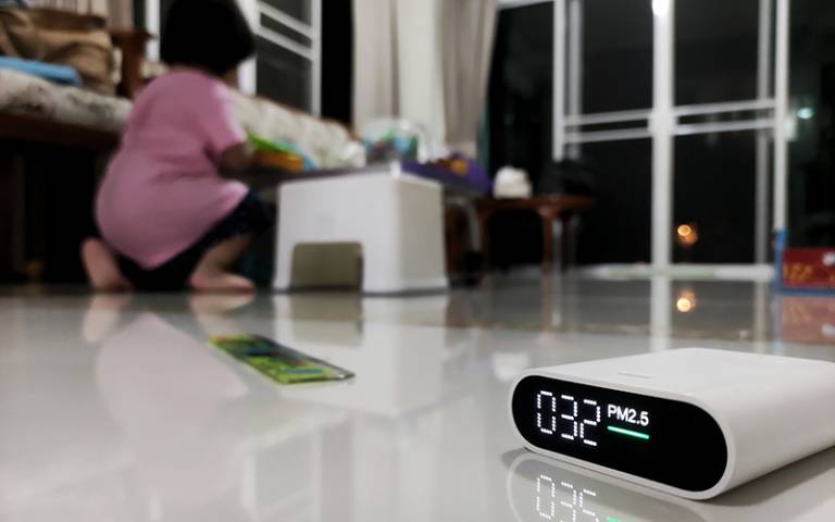A indoor air quality monitor on the floor with a child playing in the background