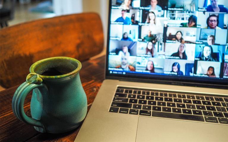 A blue mug next to a laptop with a blurred screen of a Zoom meeting