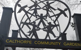 Gate of Calthorpe community garden with metal people holding hand above 