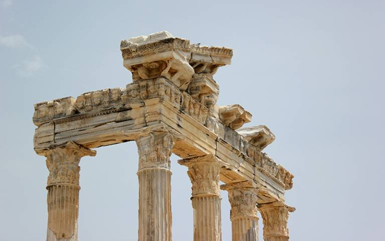 Photo shows the columns and pediment of an ancient classical temple ruin against a blue sky.