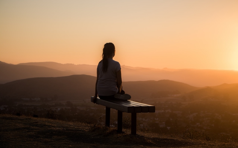 woman sitting on bench watching sunset