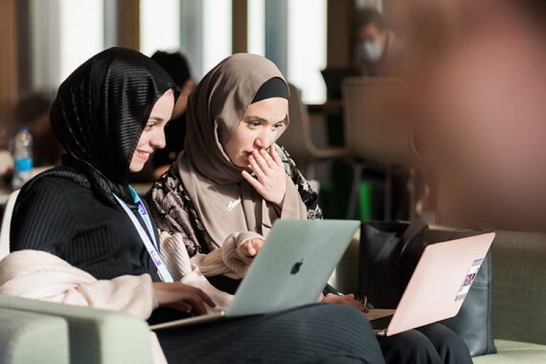 Two female students work together on their laptops 