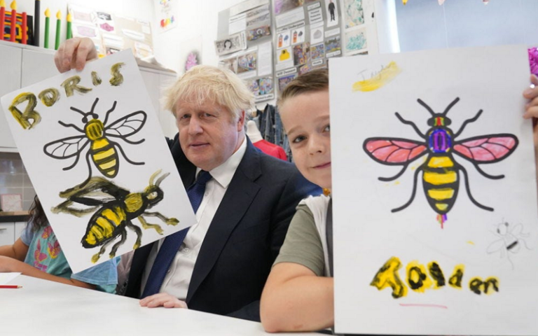 Boris Johnson holds up his Manchester Bee painting during an art class in October 2021. Photo by Stefan Rousseau-WPA Pool/Getty Images.