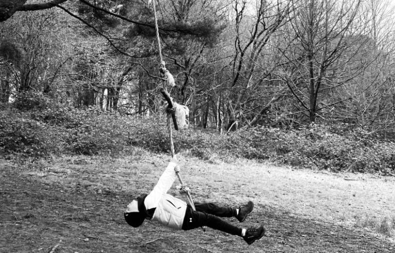 Black and white picture of child swinging on rope swing