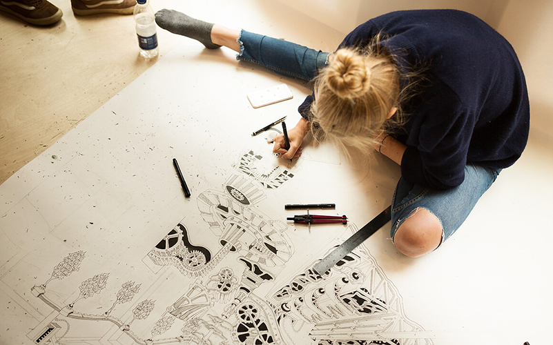 student works on large intricate drawing sat on floor