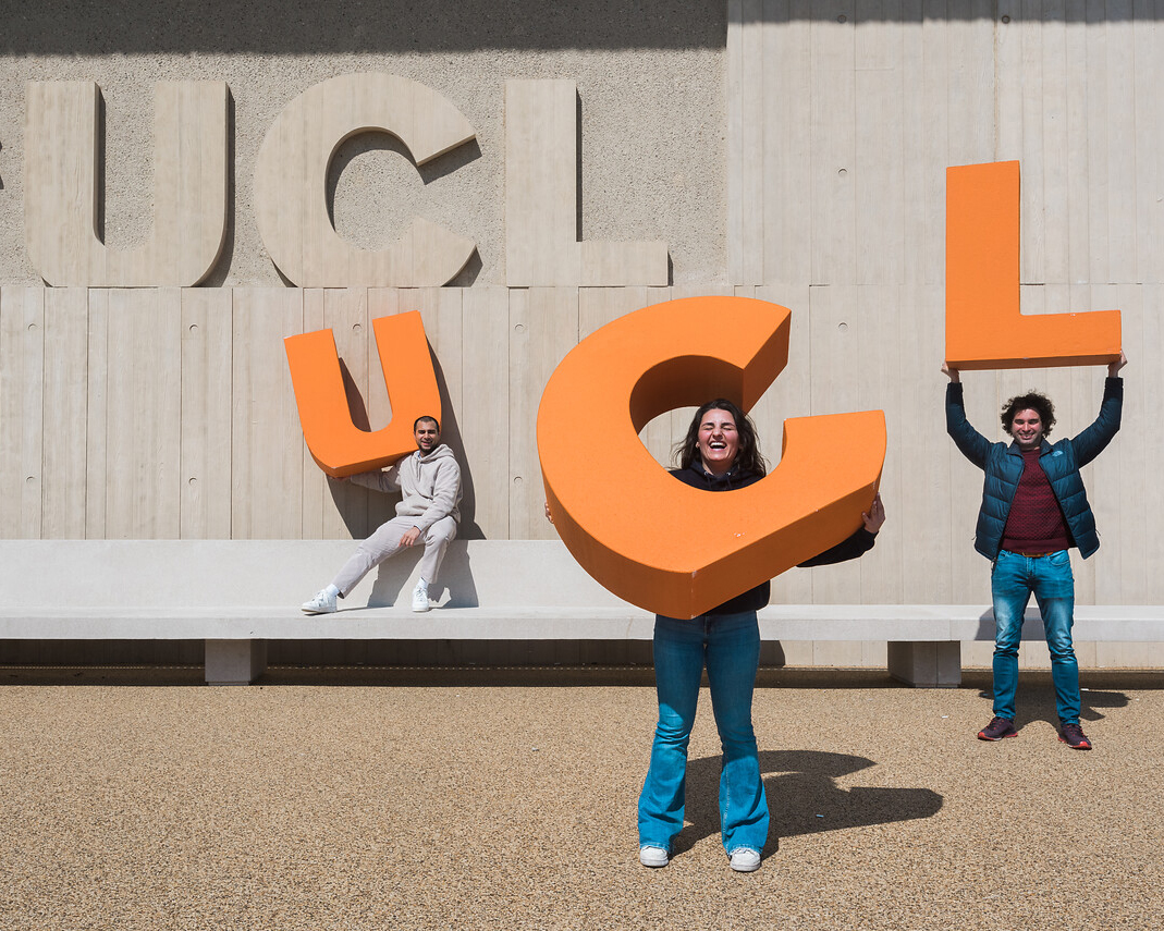 Three students holding up the letters of UCL