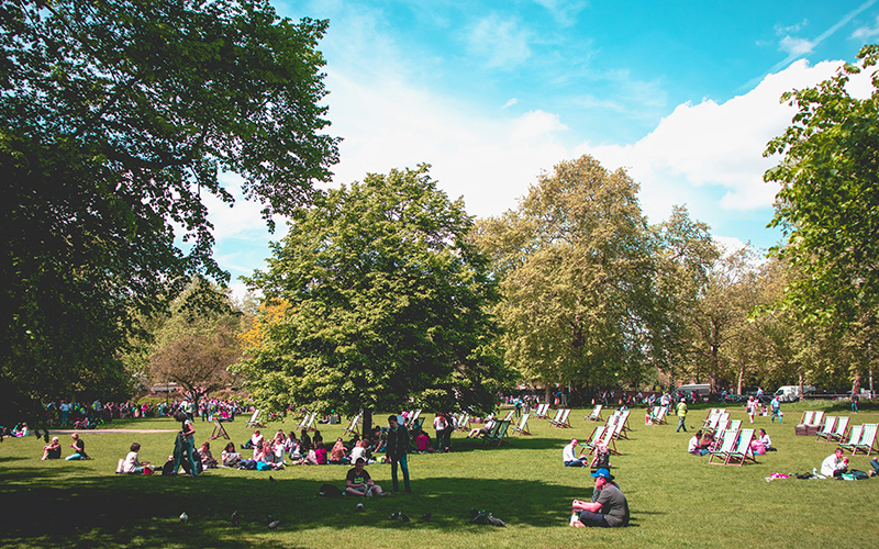 A crowded park in London with people sitting on fold out chairs and on grass
