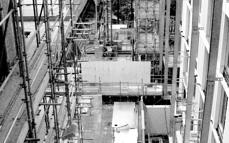 A black and white image of a building site including scaffolding and building materials