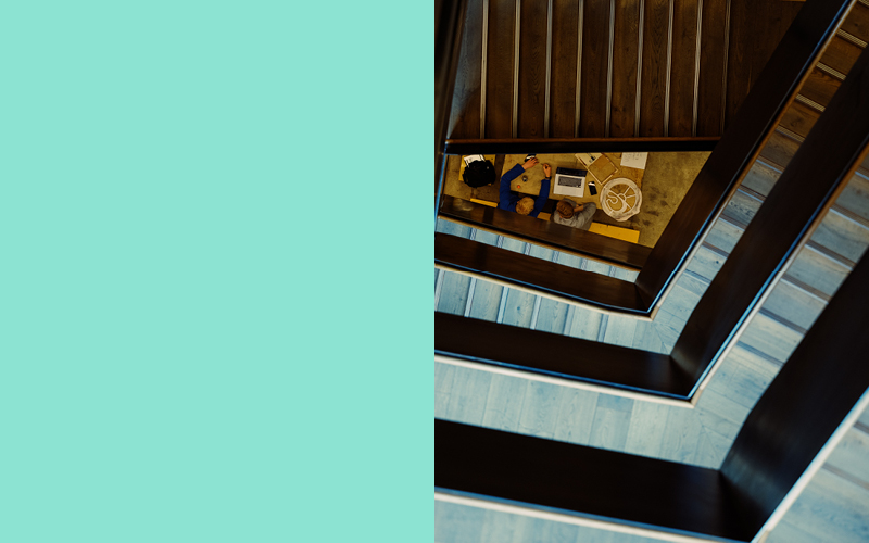 Split image of the colour turquoise and an image of the staircase at 22 Gordon Street from above with two people working on a laptop at a desk