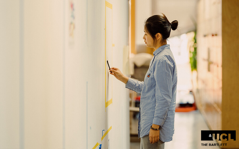 Postgraduate student standing at a white board working on a design 