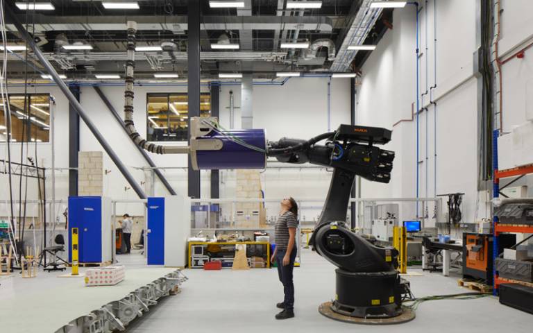 A Bartlett student stands underneath a huge robotic arm