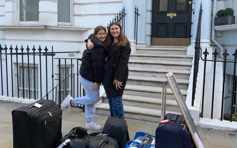 Two students standing in front of a house with a pile of luggage