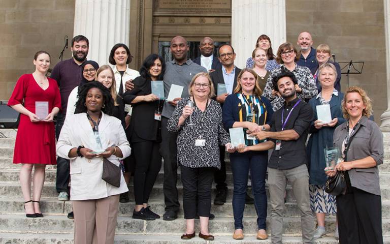 Group of UCL staff standing on stairs at main UCL campus, holding glass awards