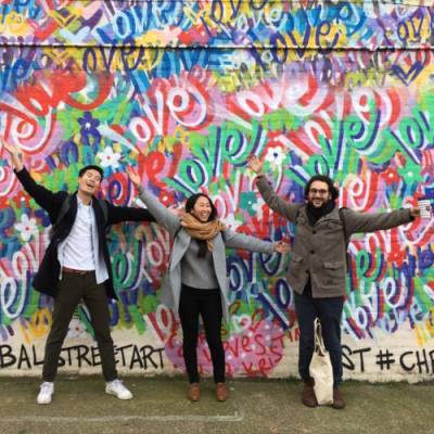 Three students posing in front of graffiti-covered wall
