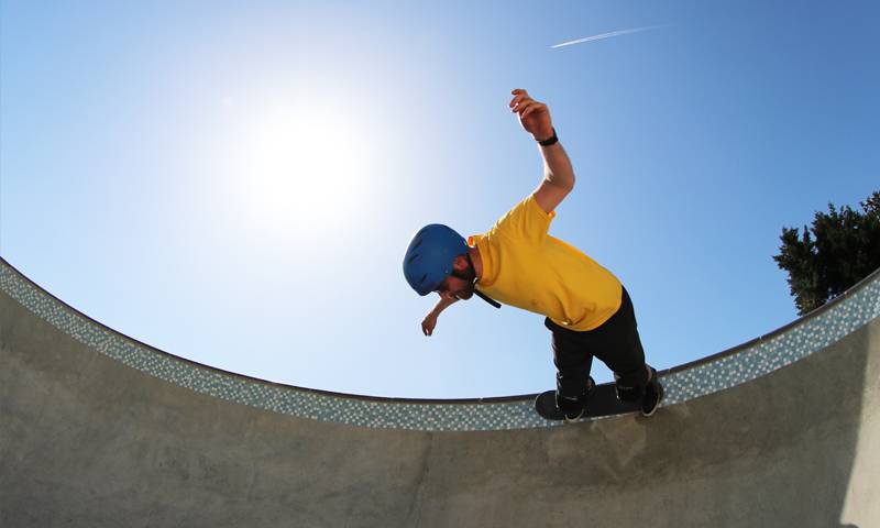 A skateboarder wearing a yellow t-shirt skates on a ramp with a clear blue sky behind