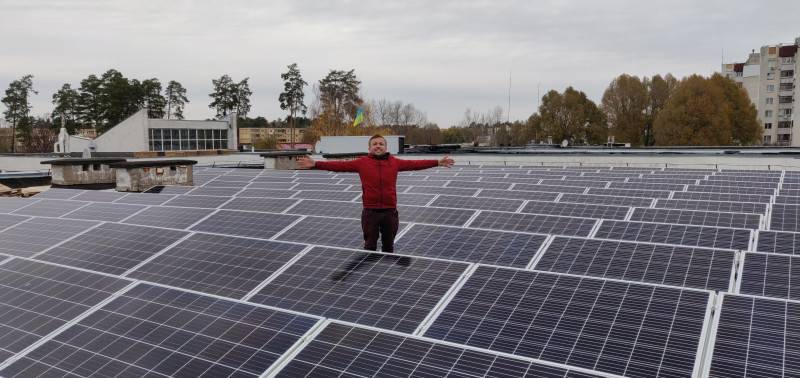 Man stands with outstretched arms among large array of solar panels