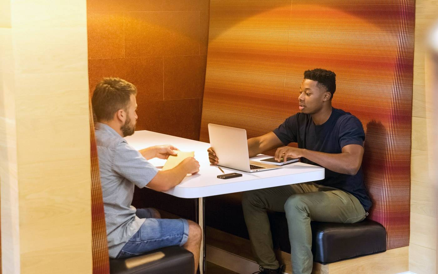 Two people sitting opposite each other, meeting in a booth with a desk between them