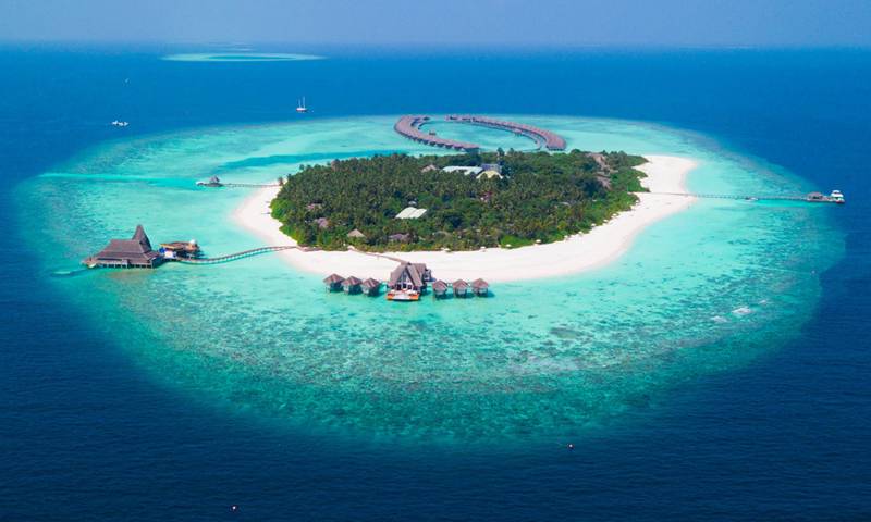 An aerial view of a largely undeveloped 'paradise' island, with white sand and surrounded by clear blue water