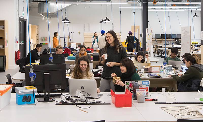 A group of students in an open-plan workshop space work around a computer