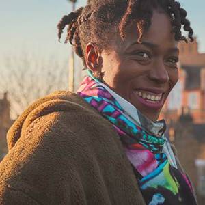 Woman smiling outside, wearing a hooded fleece jacket and multicoloured scarf