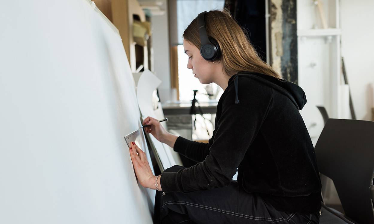 student in headphones begins drawing on large sheet of paper
