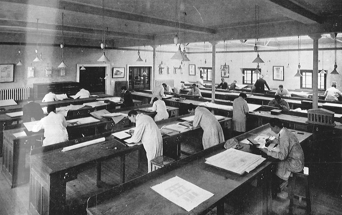 Old photo of students in long coats standing over desks
