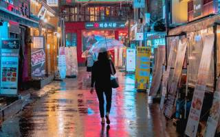 An image of a person walking down a brightly lit street in South Korea, lots of neon lights
