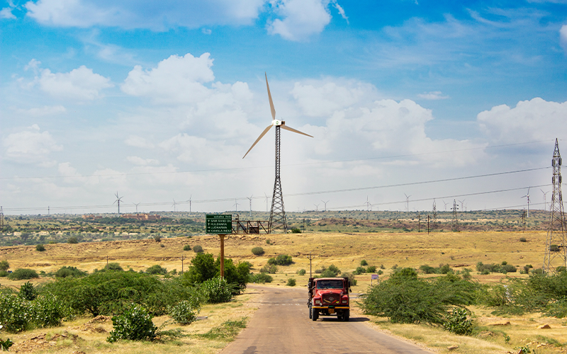 Rural landscape in India with a truck in the foreground and wind turbines and pylons in the background 