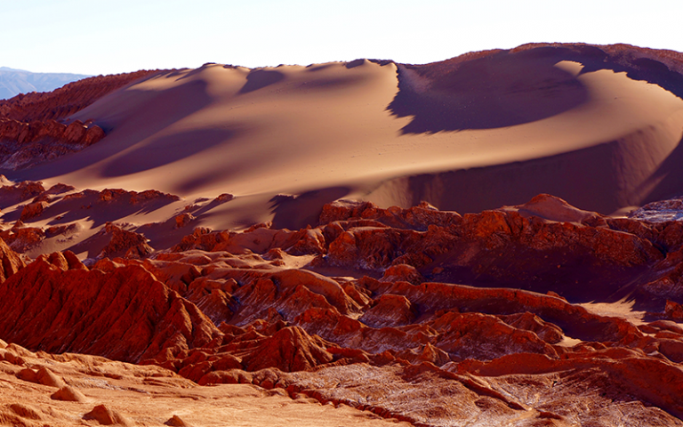 orangey rocks in the foreground with a large sand dune in the background. The Atacama desert