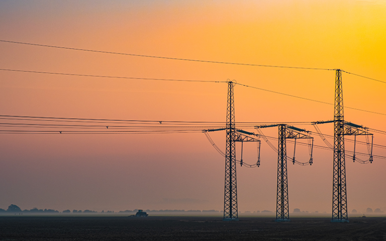 Photo shows three electricity transmission towers with a sunset in the background.