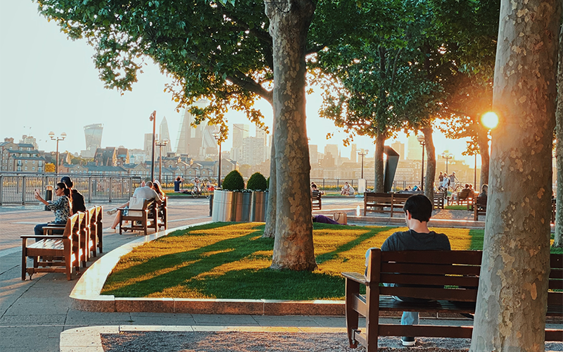 Man sitting on bench at sunset near the Thames with the City in the background 