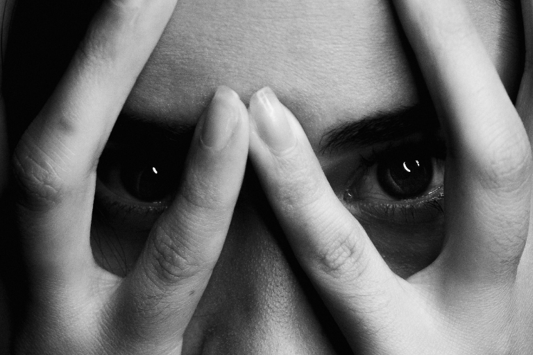 Black and white image of a person peering through their fingers.