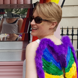 Photo of Essi, wearing pride coloured wings and smiling.