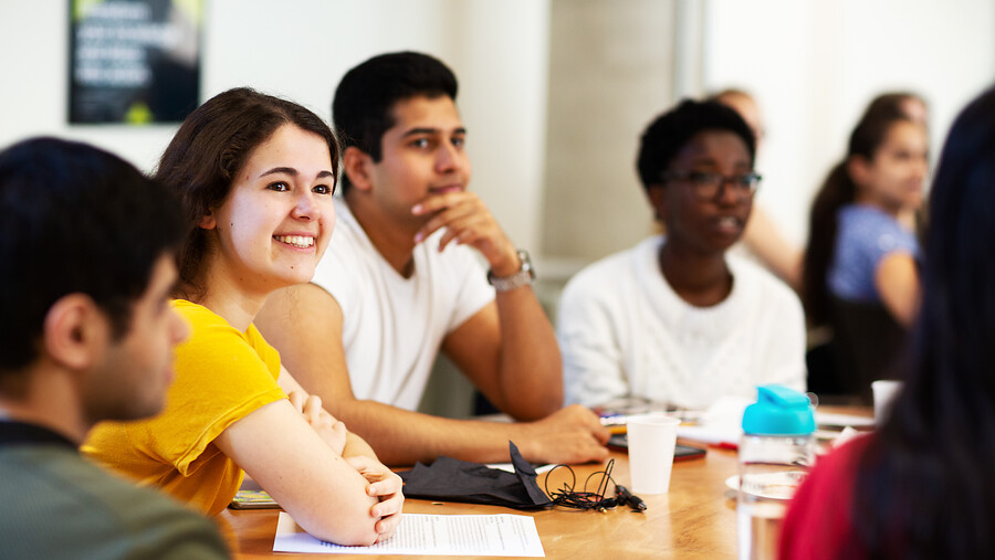 4 students sitting around a table, female student smiling.