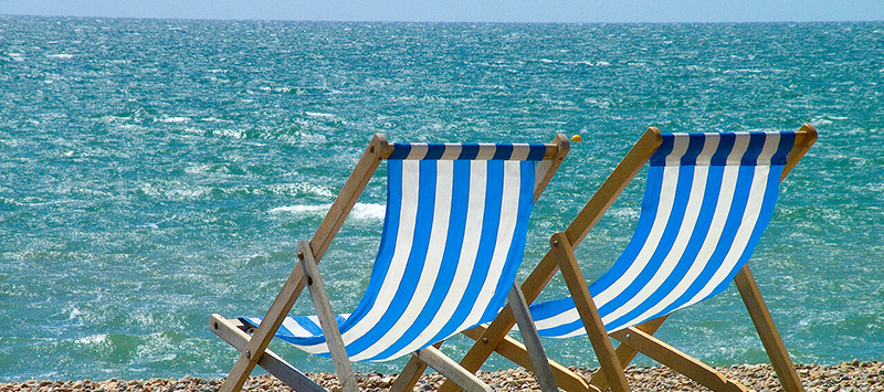 Two blue and white-striped deck chairs facing the sea on a sunny day at Brighton Beach.