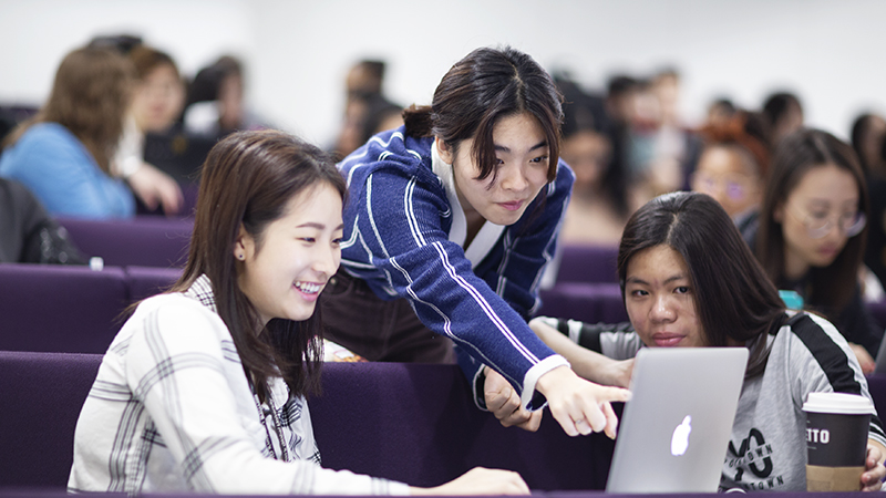 Three students looking at a laptop, the middle person is pointing at the screen