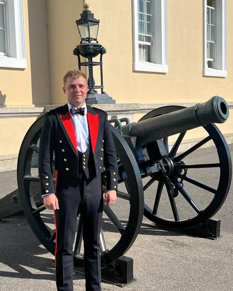 Graduate standing in front of a cannon in military uniform