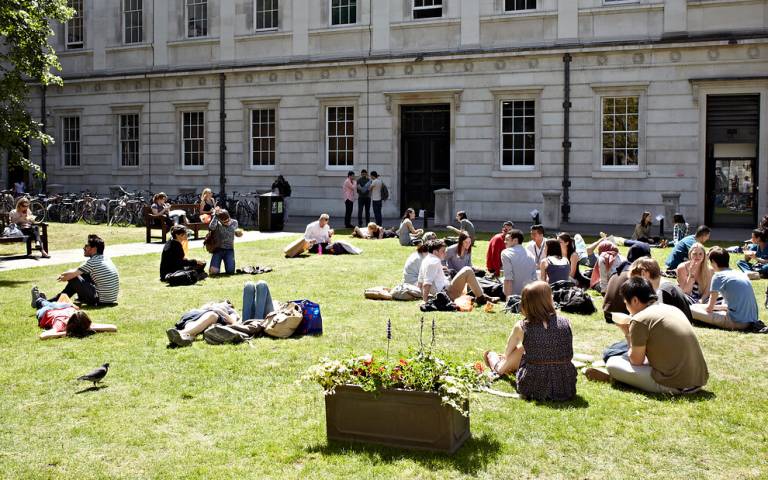 A number of students sitting down on grass at UCL's Front Quad.
