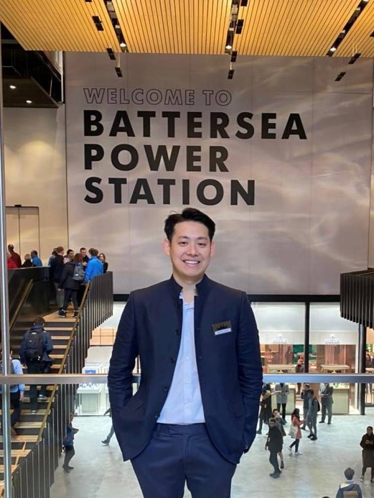 Graduate standing smiling in front the reads "Welcome to Battersea Power Station"