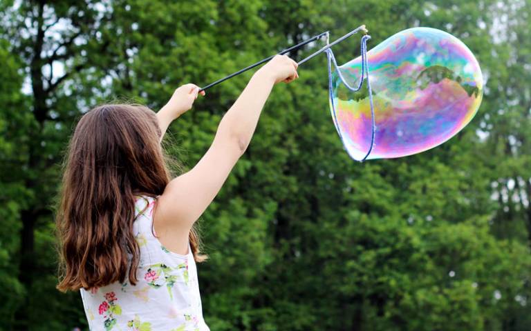 A young girl outside blowing bubbles using a kit