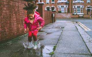 Little girl in pink raincoat and wellies jumping in puddle