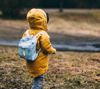 Child standing in yellow raincoat and backpack 