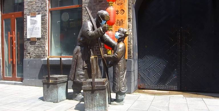 masked statues of Chinese people carrying packages