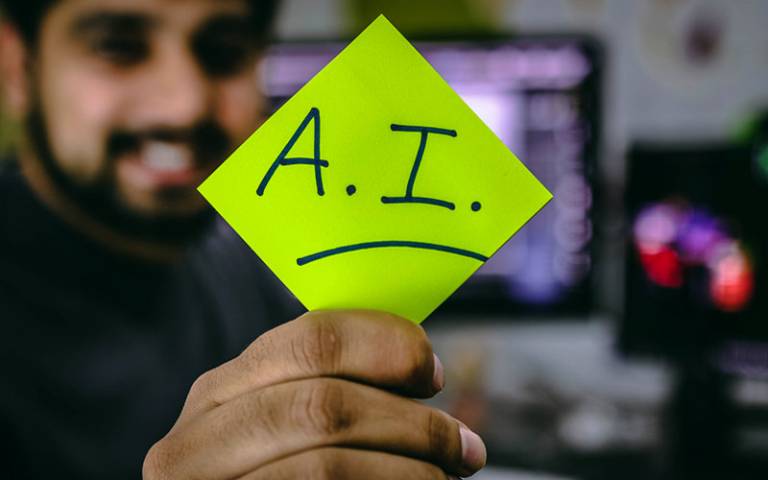 A man holding up a post-it to the screen that reads AI